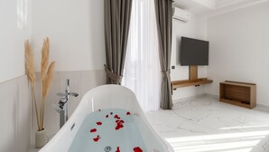 Un baño moderno con una bañera independiente, un televisor montado y un estante de madera.
