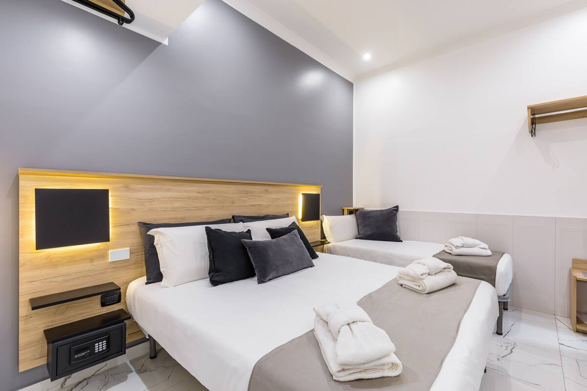 A modern hotel room with two beds, a wooden headboard, bedside tables with lamps, and a built-in TV.