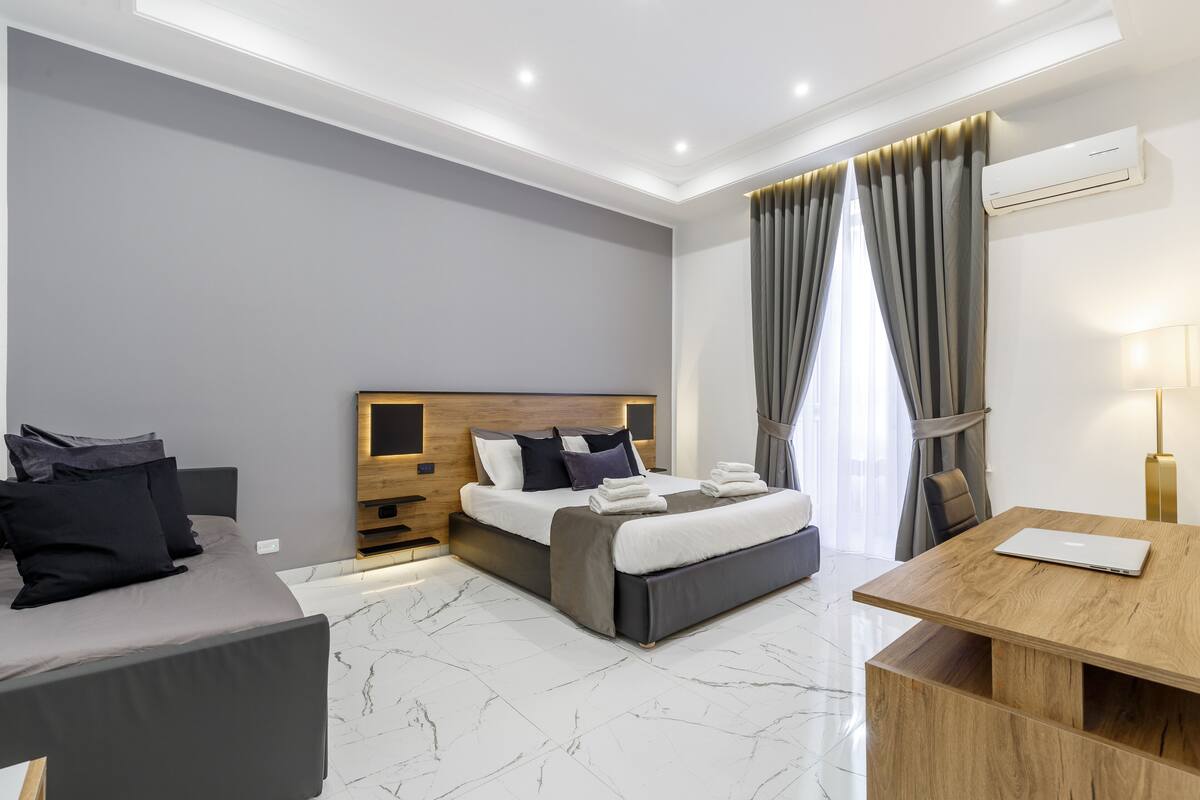 A modern hotel room with a large bed, a desk, and a seating area.