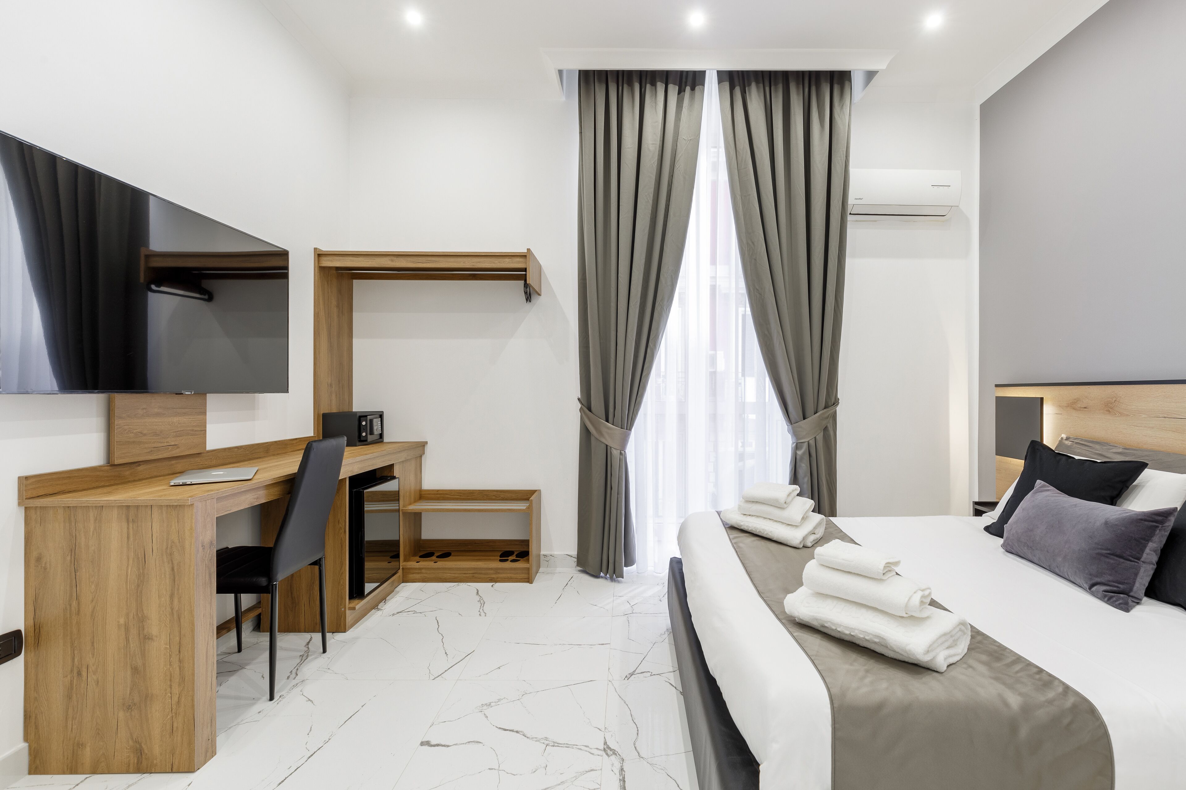 Ein modernes Hotelzimmer mit einem Holztisch, einem Sessel, einem Bett mit ordentlich gefalteten Handtüchern, einem Fernseher und einer Klimaanlage.