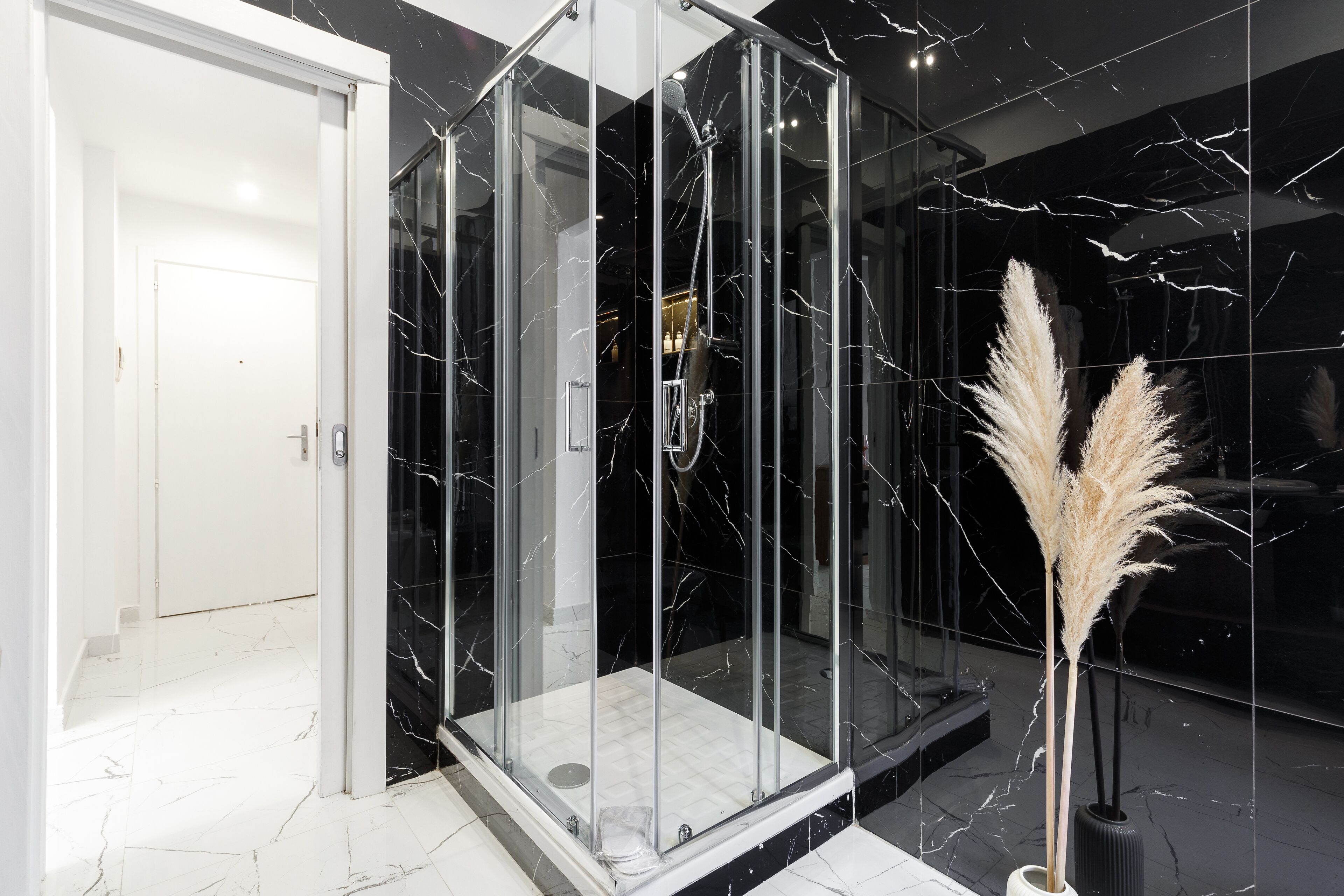 Ein modernes Badezimmer mit einer gläsernen Duschkabine, Marmorboden und einer dekorativen Vase mit Pampasgras.