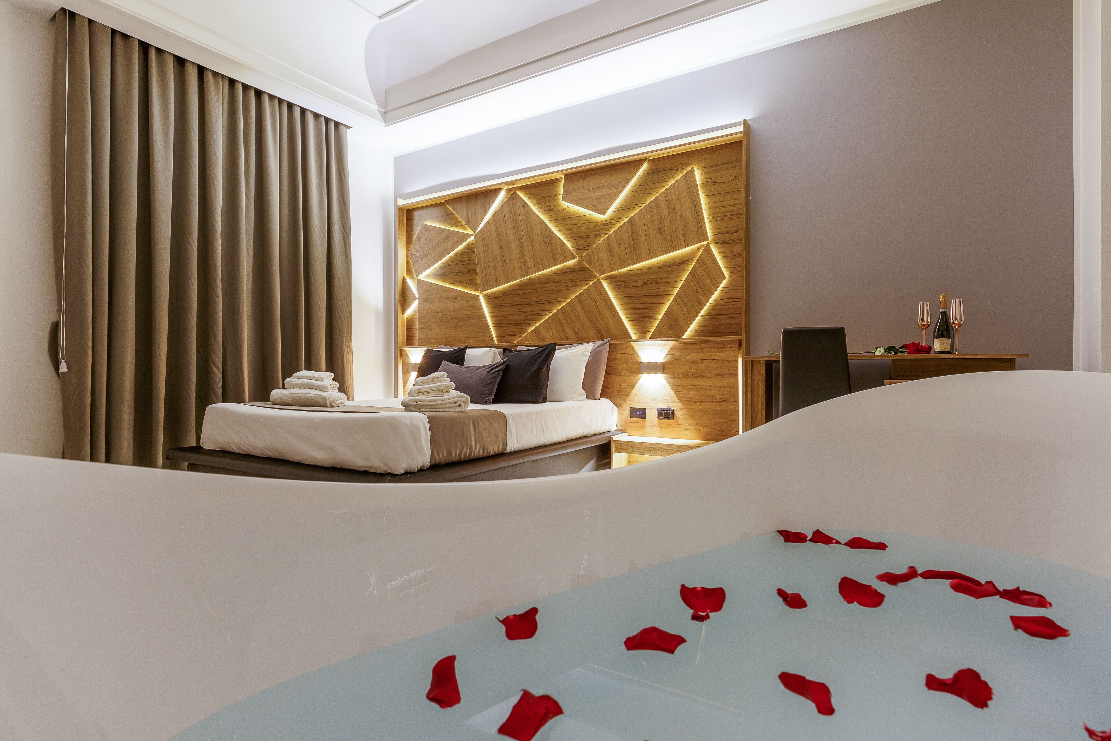 A modern hotel room with a large bathtub, a neatly made bed, and a wall-mounted light fixture.