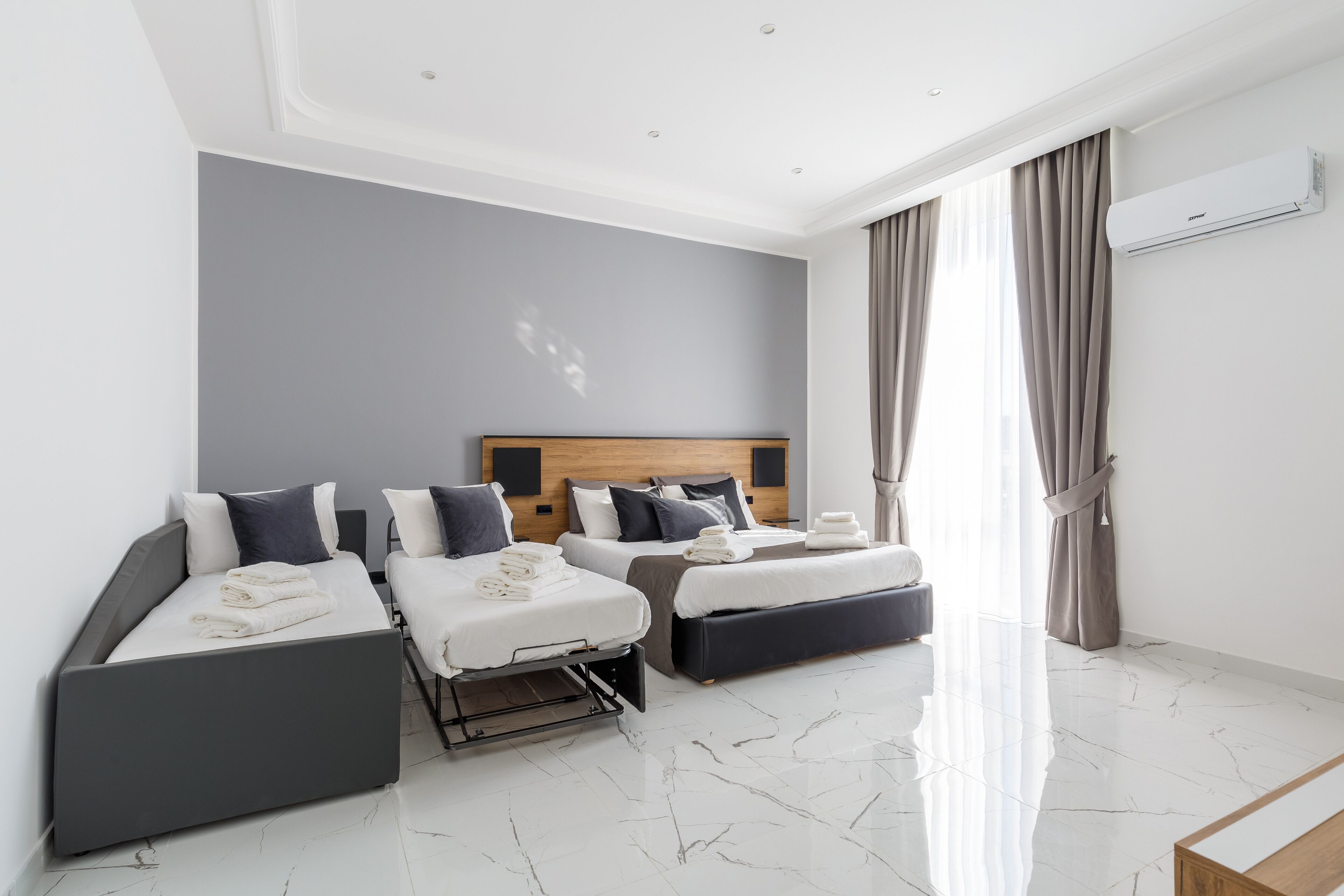A modern hotel room with a large bed, a smaller bed, and a sofa bed.