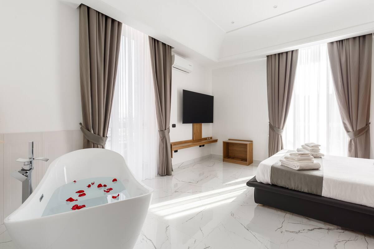 A modern hotel room with a bathtub, a bed, and a TV.