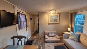 A cozy living room with a sofa, a chair, a small table, a TV, and a window with curtains.