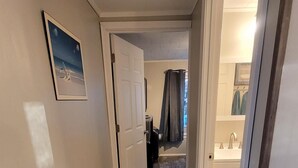 A hallway with wooden flooring, a door leading to a bathroom, and a framed picture on the wall.