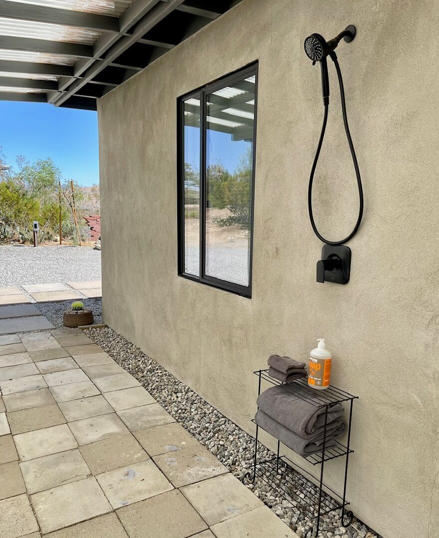 A shower area with a hose, a towel rack, and a bottle of shampoo.