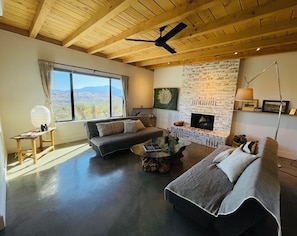 A spacious living room with a large window, a fireplace, and a ceiling fan.
