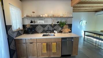 Una cocina con encimera de madera, un fregadero y lavavajillas. Hay armarios debajo de la encimera y una ventana con cortina.