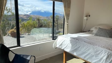 A bedroom with a large window, a bed, a chair, and a view of a landscape.