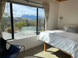 Un dormitorio con una ventana grande, una cama, una silla y vistas a un paisaje.