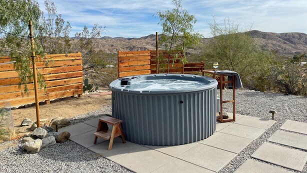 Un bain à remous dans un décor désertique, entouré de clôtures en bois et offrant une vue sur les montagnes.