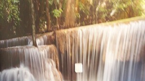Un lit recouvert d’une couverture sombre, dans une chambre avec vue sur une cascade.