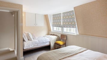 A bedroom with a single bed, a chair, a wardrobe, and a window with patterned curtains.