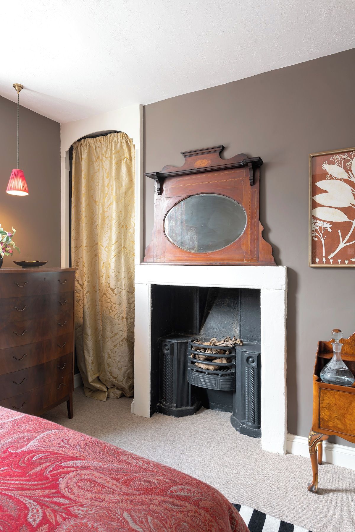 A room with a fireplace, a wooden dresser, a red lamp, and a patterned rug.