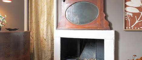 A room with a fireplace, a wooden dresser, a red lamp, and a patterned rug.