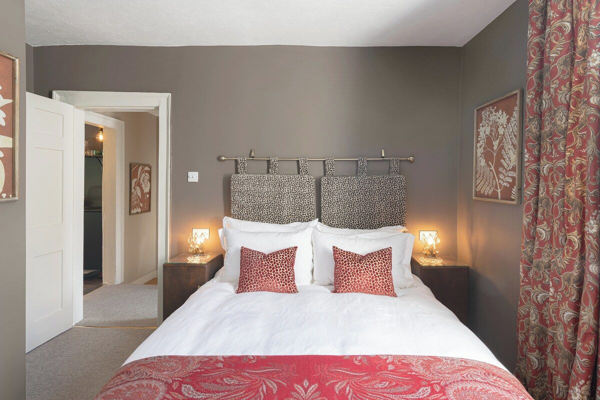 A bedroom with a bed, two bedside tables, and a door leading to another room.