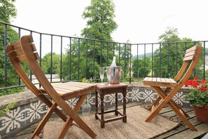 A balcony with two wooden chairs, a small table, and a potted plant.