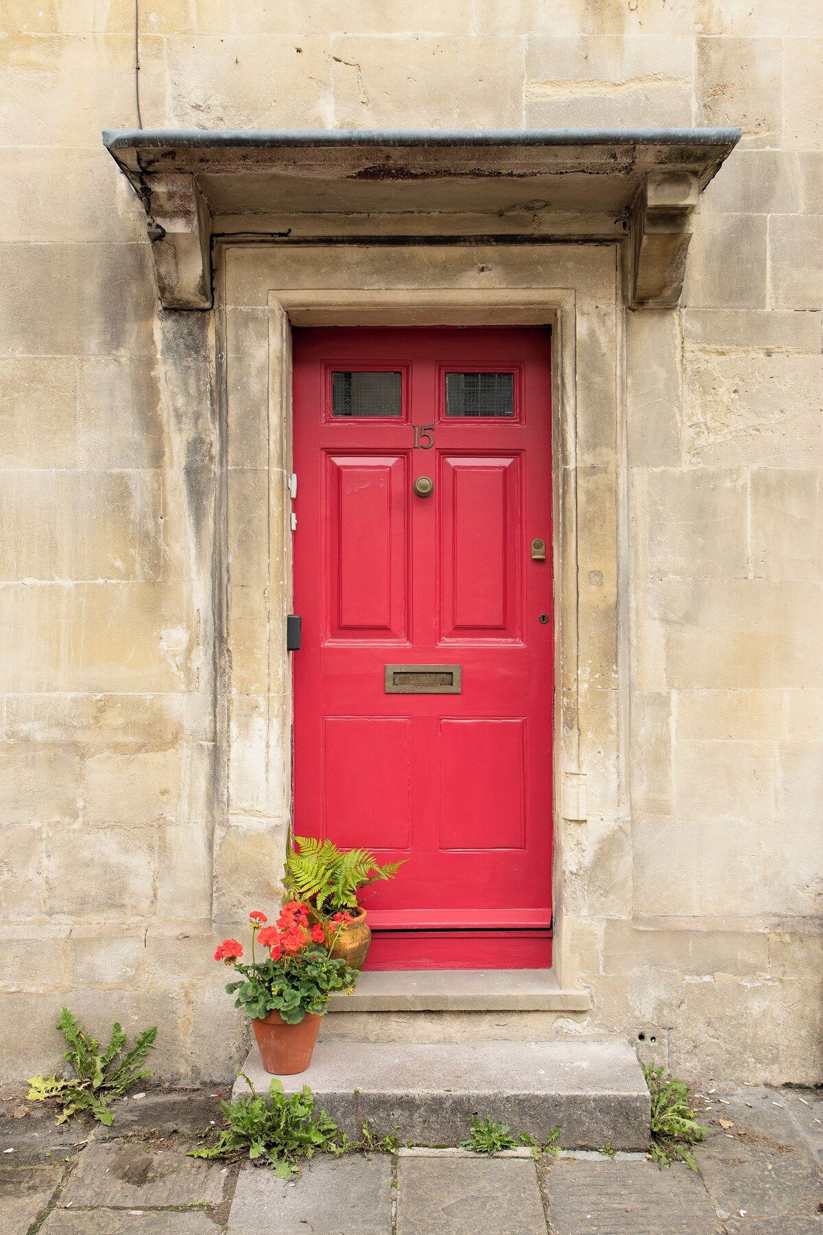 Une porte rouge, ornée d’une plaque portant un numéro, est encastrée dans un mur de pierre, et un petit marchepied permet d’y accéder.