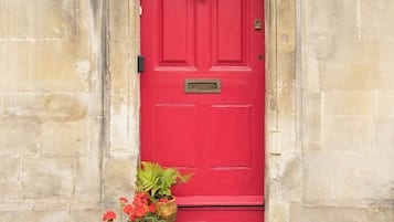 A red door with a number plate, set in a stone wall with a small step leading up to it.