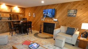 A cozy living room with a fireplace, a dining area, and a kitchen.
