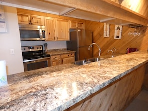 A kitchen with granite countertops, wooden cabinets, stainless steel appliances, and a built-in wine rack. - Courtside Condo at Summit (bellaire)