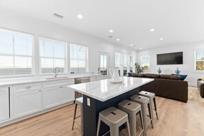 Une cuisine moderne avec des meubles blancs, un grand îlot central doté de tabourets et un téléviseur à écran plat fixé au mur.