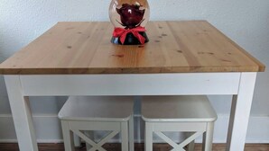 Une table en bois, deux chaises blanches, un objet décoratif posé sur la table et un mur sobre en arrière-plan.