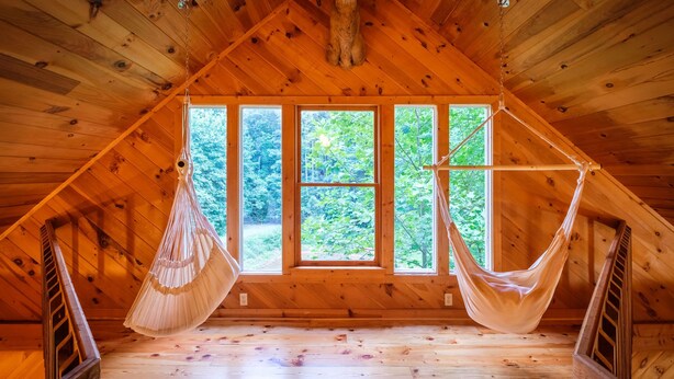 Quarto de sótão rústico com teto inclinado, amplas janelas e duas redes.
