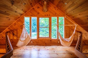 A wooden attic room with a sloped ceiling, large windows, and two hammocks. - Orchard Mountain Cabin, Enchanting Retreat – Exclusive Lakefront Sanctuary (Ellijay)