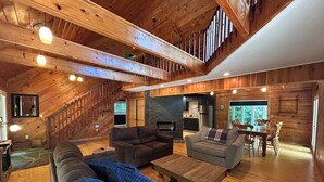Um loft espaçoso com pé-alto, vigas de madeira, área de refeições com mesa e cadeiras, sofá e cozinha equipada com eletrodomésticos modernos.