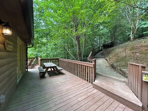 Una terraza de madera con mesas y sillas de picnic, rodeada de un bosque denso.