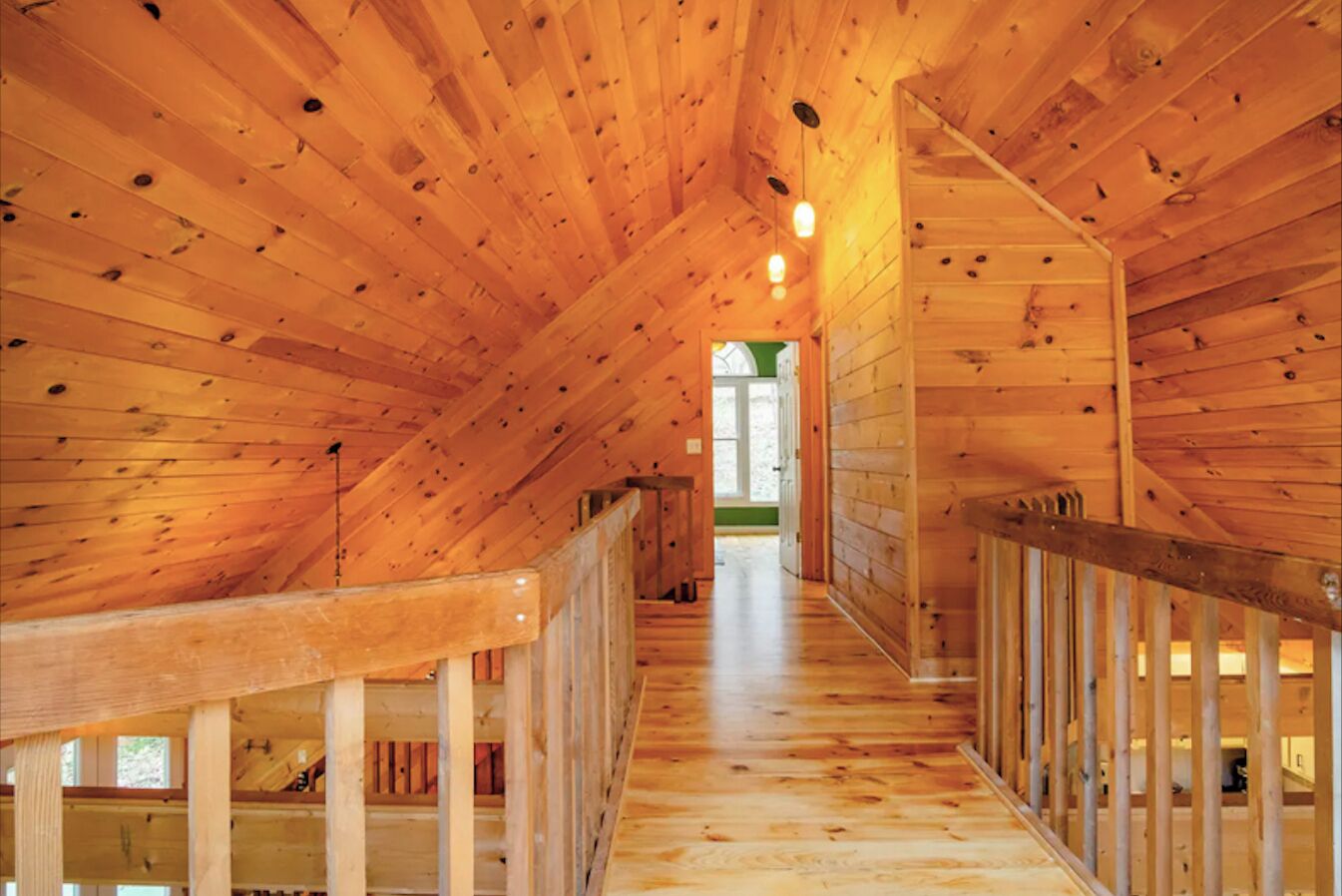 Un intérieur en bois avec un plafond incliné, des rampes d’escalier en bois et un escalier apparent menant à un niveau supérieur.