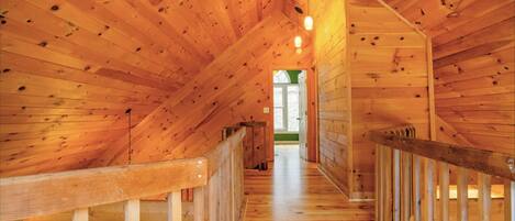 Un intérieur en bois avec un plafond incliné, des rampes d’escalier en bois et un escalier apparent menant à un niveau supérieur.
