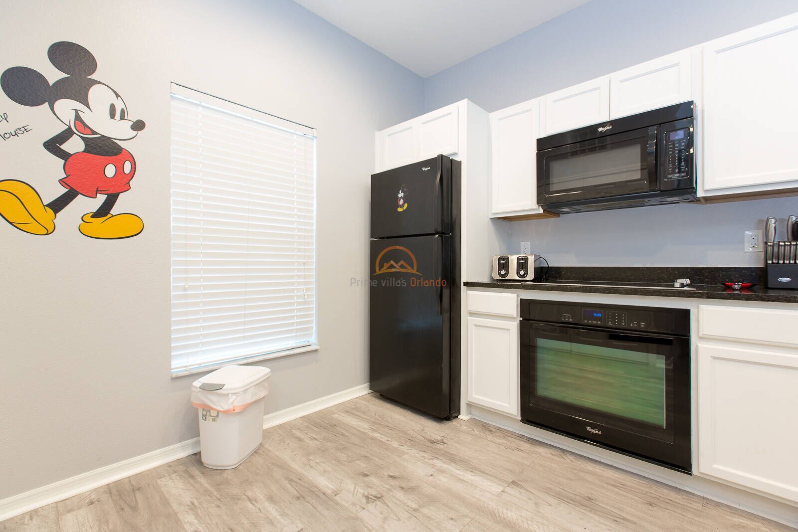 A modern kitchen with white cabinets, a black refrigerator, a microwave, an oven, and a trash bin.