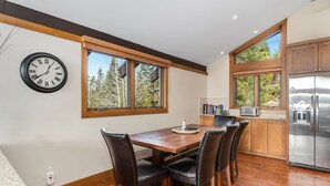Une cuisine moderne avec une table à manger en bois, des chaises noires, une horloge et un grand réfrigérateur.