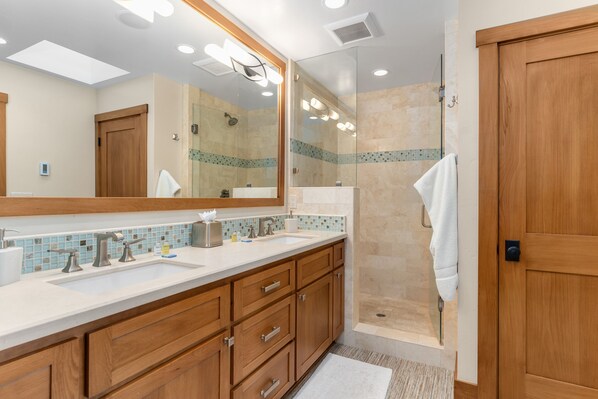 A modern bathroom with a large mirror, two sinks, wooden cabinets, and a glass-enclosed shower area. - The Pear House - Beautiful Dollar Point Home with Tahoe Views, Private Hot Tub, Pool Table (Tahoe City)