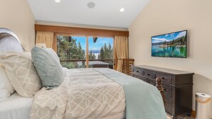 Une chambre à coucher avec un lit, une commode, un tableau et une vue sur un lac, visible à travers de grandes fenêtres.