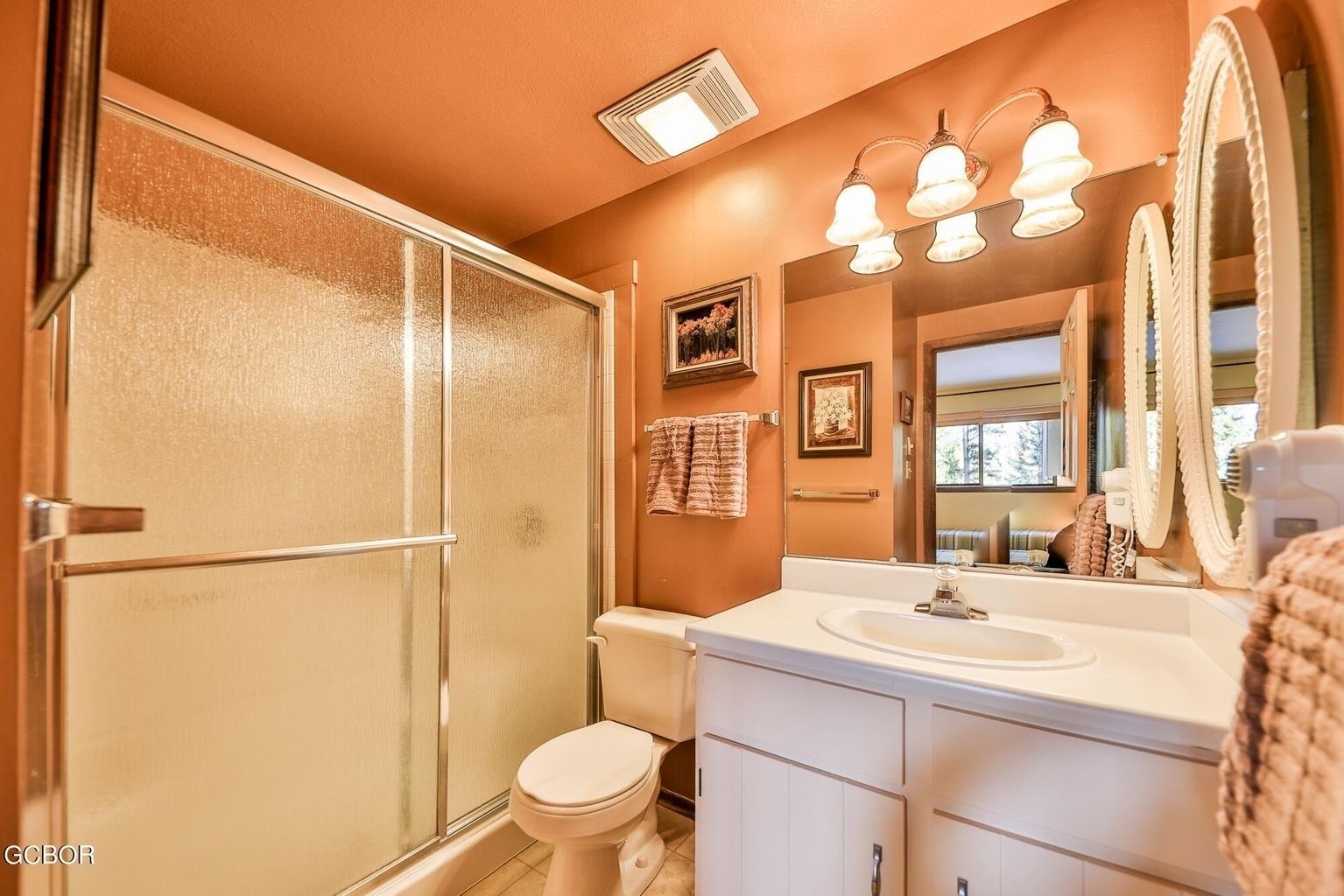 A bathroom with a glass shower door, a toilet, a sink with a mirror, and a towel rack.