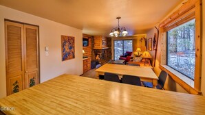 Un interior acogedor de cabaña con una mesa de comedor, sillas, una chimenea y un ventanal con vistas al exterior.