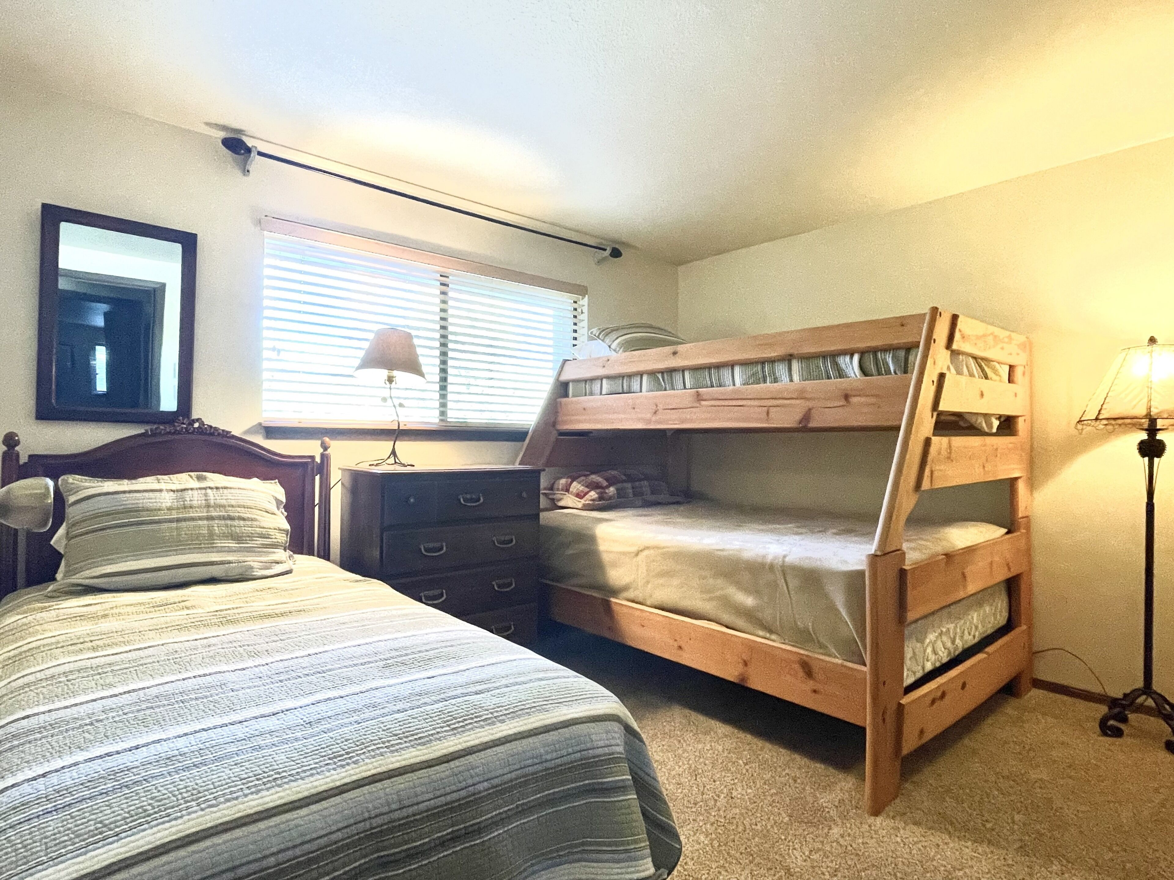 A bedroom with a bunk bed, a single bed, a dresser, and a lamp.