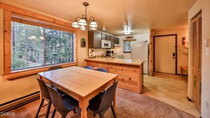 Una cocina acogedora con una mesa y sillas de madera, un ventanal con vistas a un bosque y un microondas moderno.