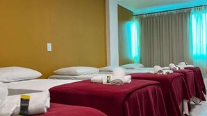 Habitación de hotel con varias camas cubiertas con ropa de cama roja, almohadas blancas y toallas dobladas con cuidado.