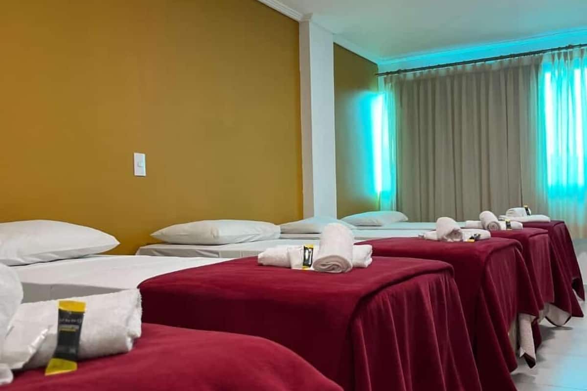 Habitación de hotel con varias camas cubiertas con ropa de cama roja, almohadas blancas y toallas dobladas con cuidado.