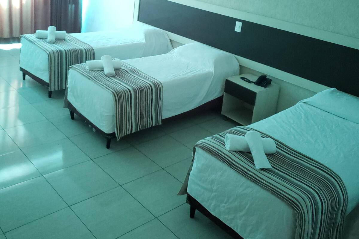 Una habitación de hotel con dos camas individuales, una mesita de noche pequeña con teléfono y un ventanal con cortinas.