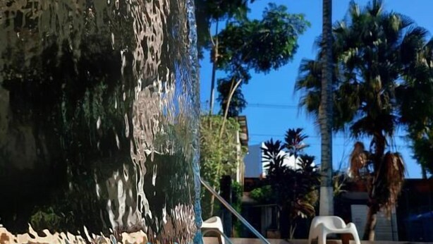 Una piscina con agua cristalina, una cascada y palmeras al fondo.