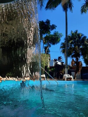 A pool with clear water, a waterfall feature, and palm trees in the background.