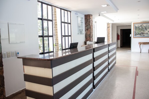 A reception desk with a modern design, a large window, and a wall-mounted information board.