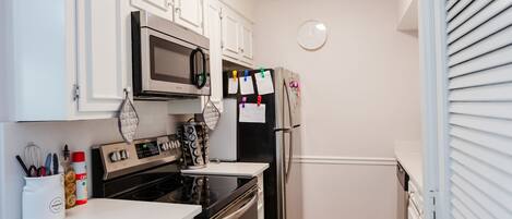 A compact kitchen with white cabinets, a microwave, a stove, and a refrigerator.