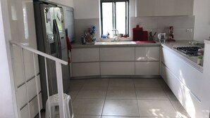 Une cuisine moderne avec des meubles blancs, un réfrigérateur en acier inoxydable, une cuisinière à gaz et une fenêtre qui laisse entrer la lumière naturelle.